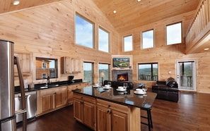 Cozy cabin with a central island kitchen, large windows, and a fireplace.