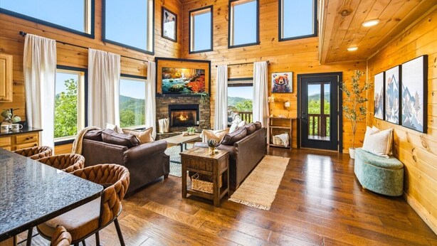 A spacious living room with a fireplace, wooden walls, large windows, and a cozy seating area. - Amazing Mountain View, Hot Tub, Game Room! (Sevierville)