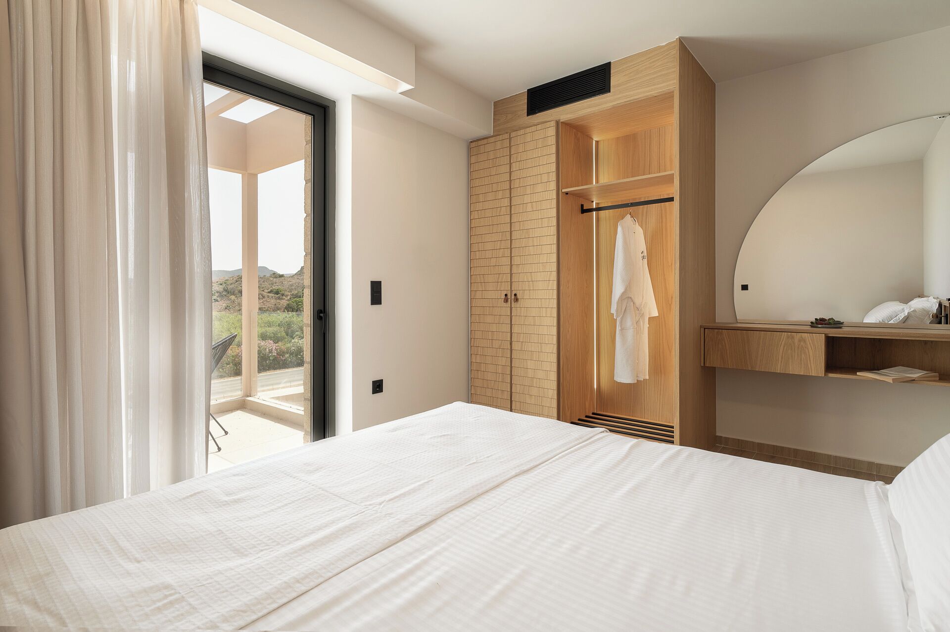 Un dormitorio con una cama grande, un armario, un espejo y vistas al exterior.