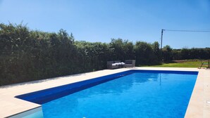 Ein rechteckiger Pool mit gefliestem Rand, umgeben von einer Hecke und einer Rasenfläche.