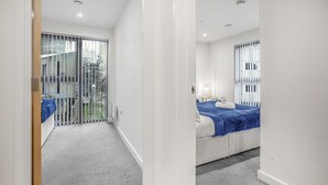 A hotel room with a large sliding glass door leading to a balcony, a bed with a blue bedspread, and a small bedside table with a lamp. - 2 Bed Apt Sleeps 7 - Arcade Machine, Wifi, Central (Birmingham)