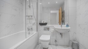 Ein modernes Badezimmer mit einer Glaskabine zur Dusche, einer weißen Toilette, einem Waschbecken mit Spiegel und einem Mülleimer.