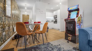 A modern kitchen with white cabinets, a dining area with orange chairs, and a retro arcade machine. - 2 Bed Apt Sleeps 7 - Arcade Machine, Wifi, Central (Birmingham)