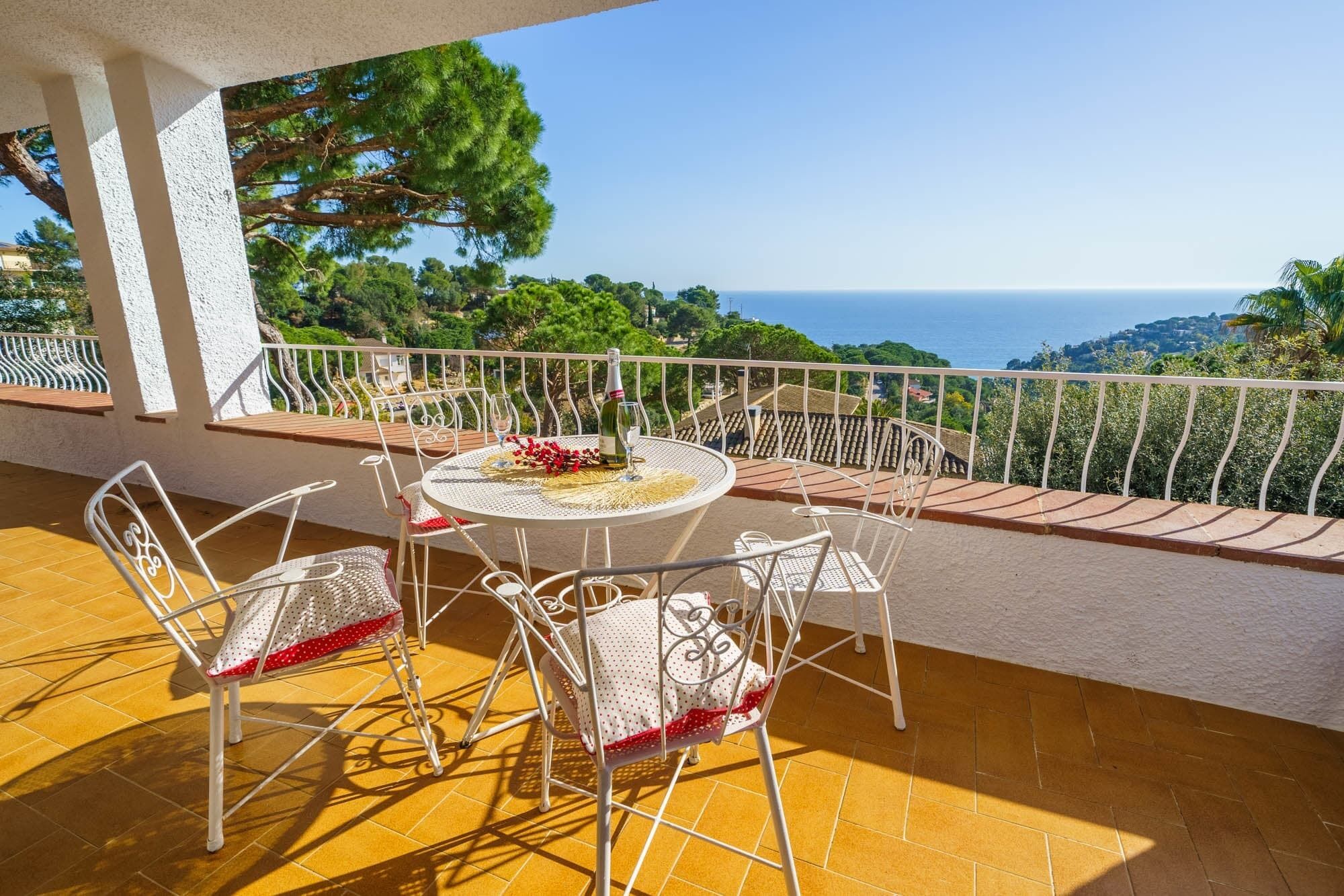 Een terras met een ronde tafel en stoelen, een fles wijn en uitzicht op zee.