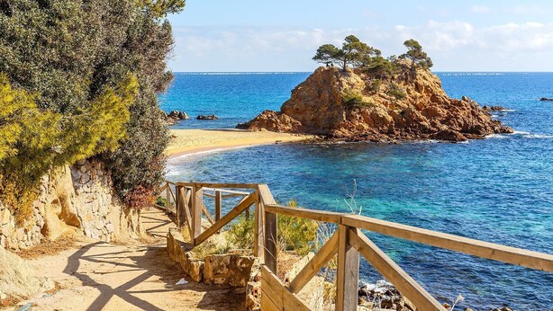 Un sendero costero que lleva a una playa con aguas azules cristalinas y afloramientos rocosos.