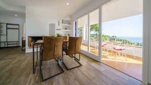 Una sala de estar moderna con comedor, amplias puertas de vidrio correderas que dan a un balcón con vistas al mar.