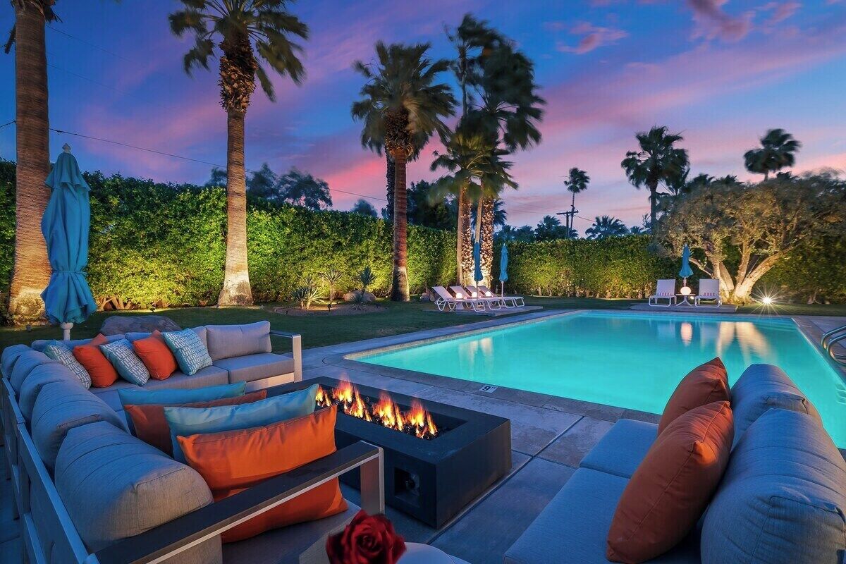 A poolside area with a fire pit, lounge chairs, and a sofa with cushions.