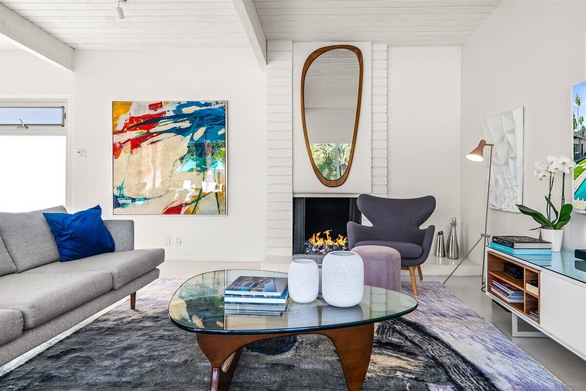 A modern living room with a glass coffee table, a gray sofa, a fireplace, and a large abstract painting.