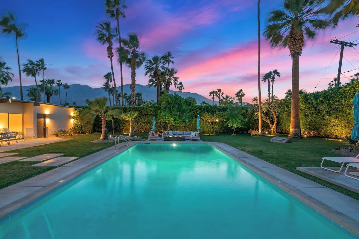 A swimming pool with a sunset view, surrounded by palm trees and a well-maintained lawn.