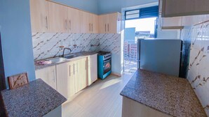 Una cocina con armarios de madera clara, salpicadero de mármol, un lavabo, una estufa y un refrigerador.