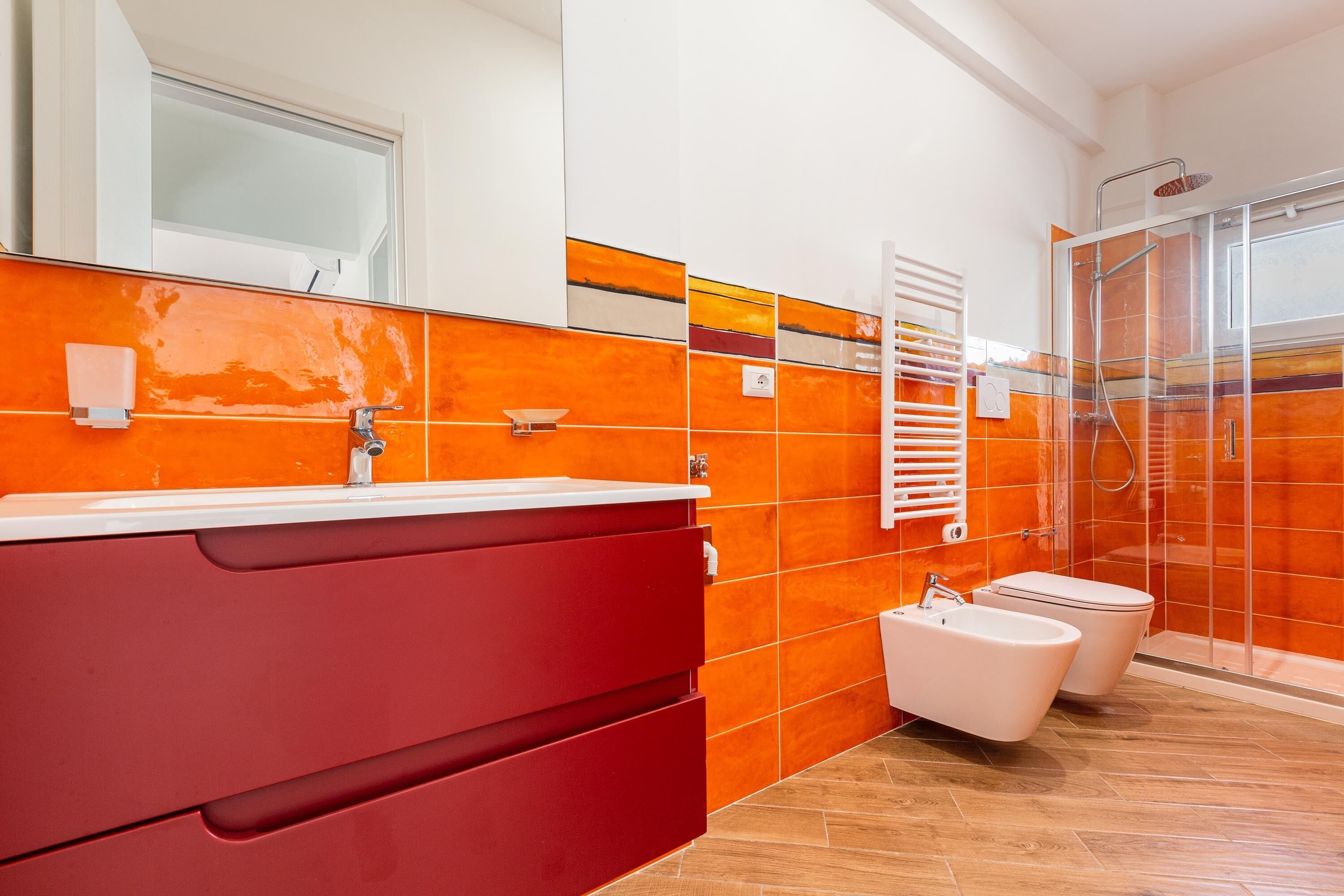A modern bathroom with a red vanity, a glass shower enclosure, and a white toilet.