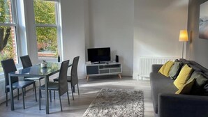A modern living room with a dining area, a flat-screen TV, and a sofa with cushions. - Spacious 2-bed Queens by CityGo (Belfast)