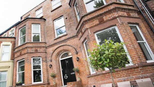 A brick building with a black front door, multiple windows, and a small tree in front. - Spacious 2-bed Queens by CityGo (Belfast)