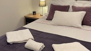 A neatly made bed with a purple bedspread, two white pillows, and two folded white towels. - Spacious 2-bed Queens by CityGo (Belfast)