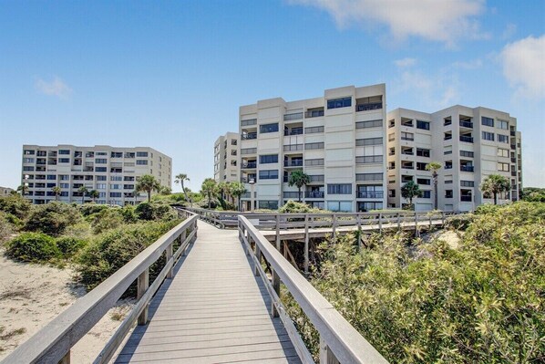 Une promenade en bois mène à un hôtel situé en bord de mer, doté de plusieurs étages et de balcons.