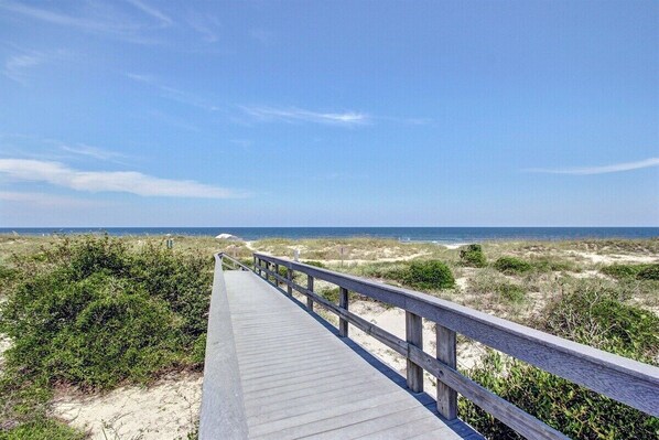Une promenade en bois menant à une plage bordée de dunes et d’une végétation clairsemée.