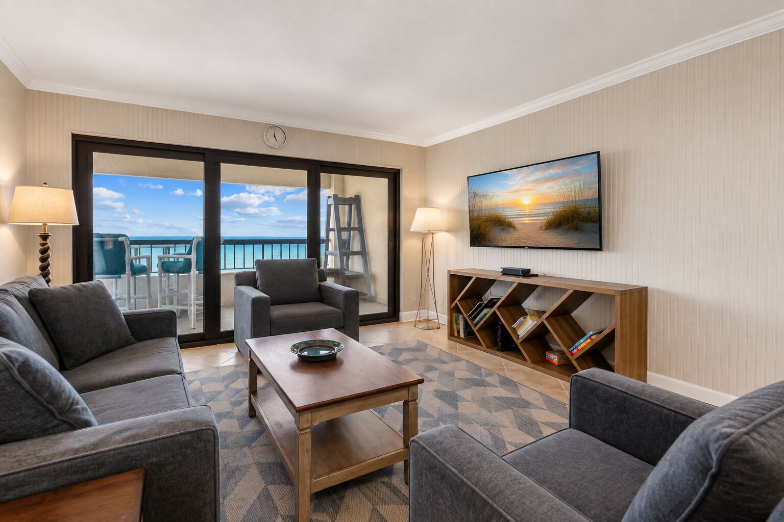 Habitación de hotel con balcón, sofá, mesa de centro, televisor y estantería.