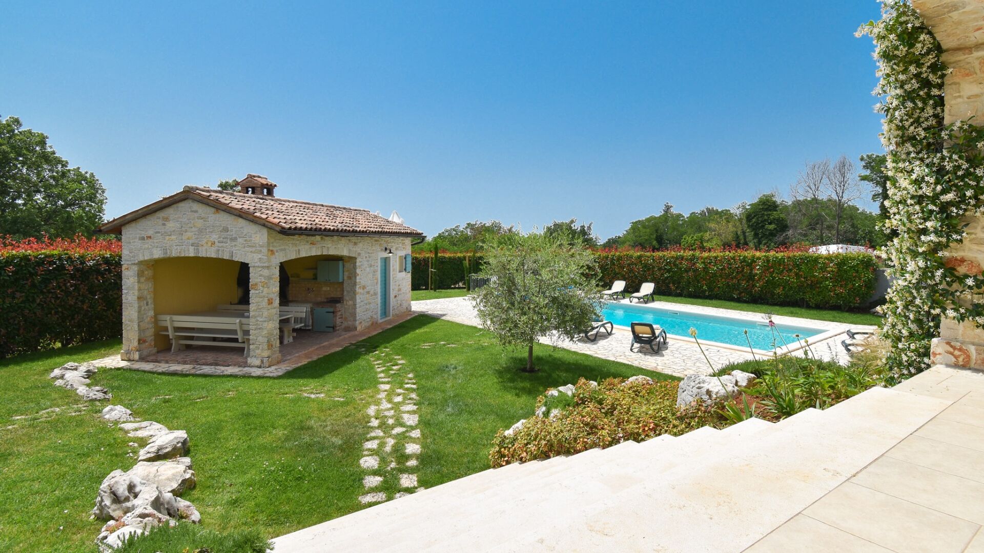 A stone cottage with a pool, surrounded by a well-maintained lawn and hedges.