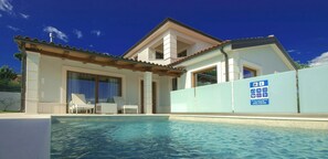 A modern house with a swimming pool, a covered patio with lounge chairs, and a blue sign indicating amenities. - Villa Gloria Vita by Villas Guide (Brtonigla)