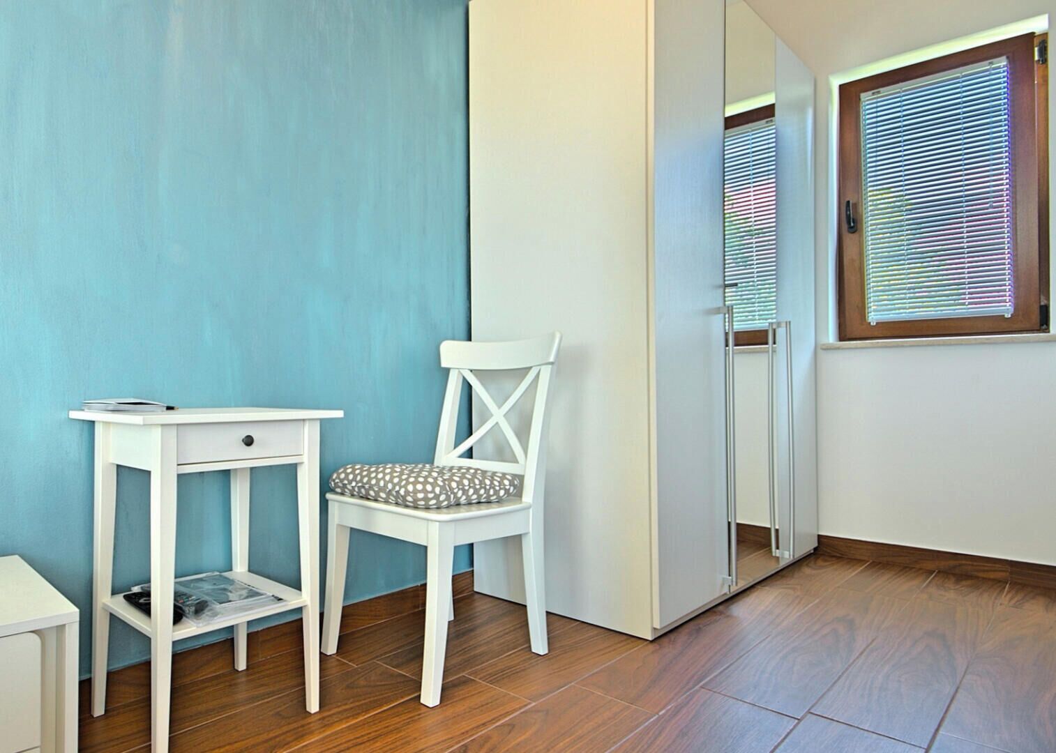 A room with a white chair, a small white table, and a window with blinds.