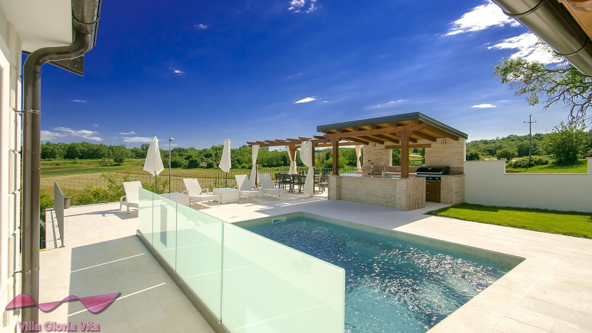 A modern outdoor pool area with a pergola, lounge chairs, and a barbecue area.