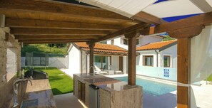 Un espace extérieur abrité comprenant une piscine, un barbecue et un coin salon avec des fauteuils confortables.