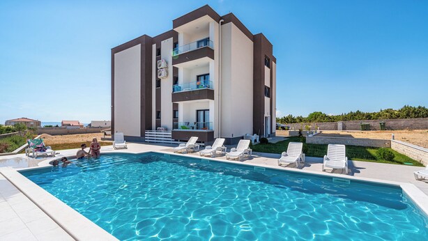 A modern building with a swimming pool, multiple balconies, and sun loungers. - Cozy Studio Villa Laura 5 (Novalja)