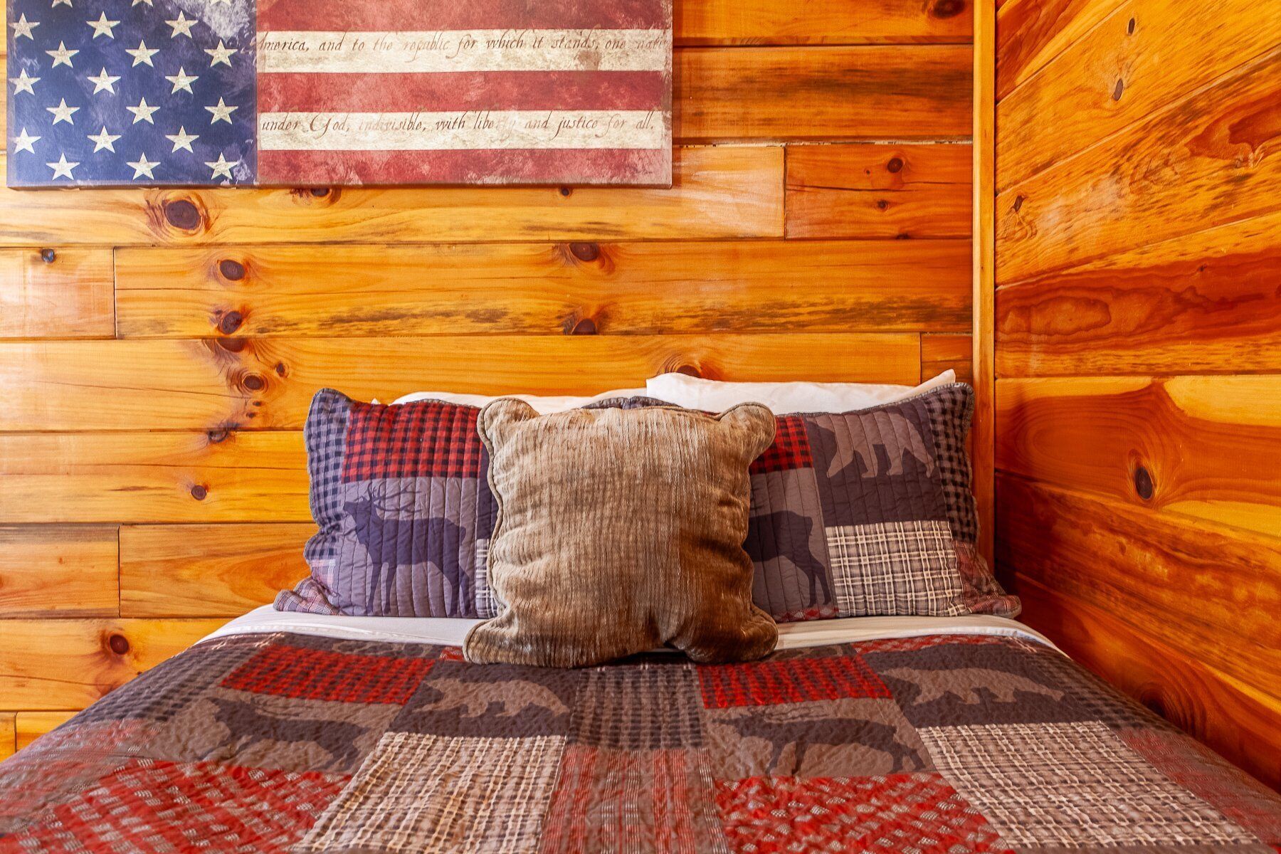 L’intérieur d’un chalet en bois, avec un lit agrémenté d’une couverture matelassée et de deux coussins décoratifs.