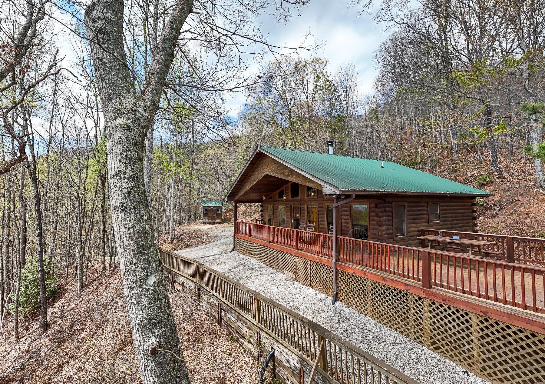 A wooden cabin with a green roof, surrounded by a wooden deck and a gravel path.