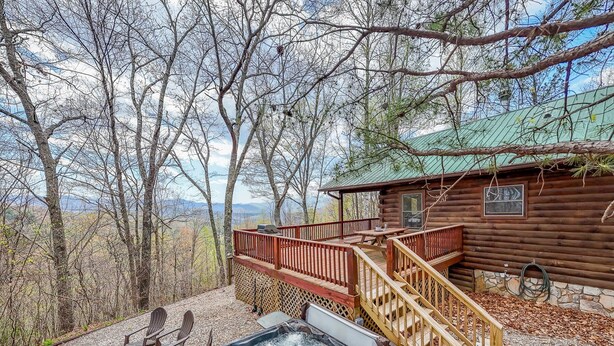 Un chalet rustique doté d’un bain à remous et d’une terrasse, entouré d’arbres et offrant une vue sur un paysage montagneux.
