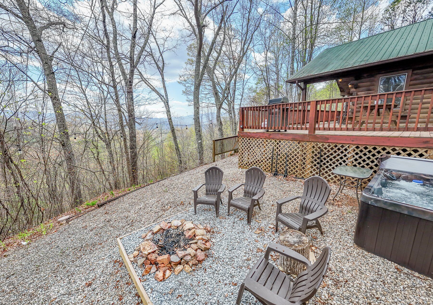 Um terraço com cadeiras Adirondack e um poço de fogo, com vista para uma área arborizada.