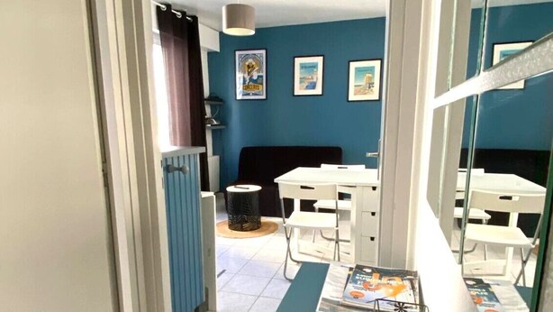A room with a blue wall, a white door, a dining table with chairs, and a window with curtains.