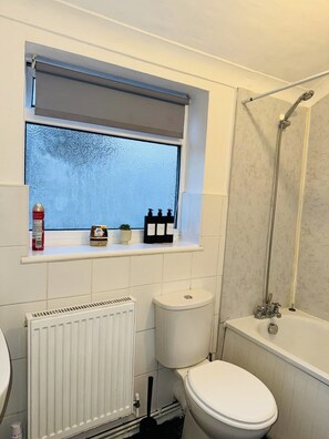 A bathroom with a toilet, a radiator, a window with a shelf, and a shower area. - 3 bed House in Portsmouth (Portsmouth)