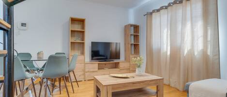 Una sala de estar moderna con una mesa de centro de madera, sillas grises, un televisor de pantalla plana y estanterías empotradas de madera.