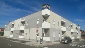 A modern building with multiple balconies, a speed limit sign, and a car parked in front. - Polorooms Vara (Zaratan)
