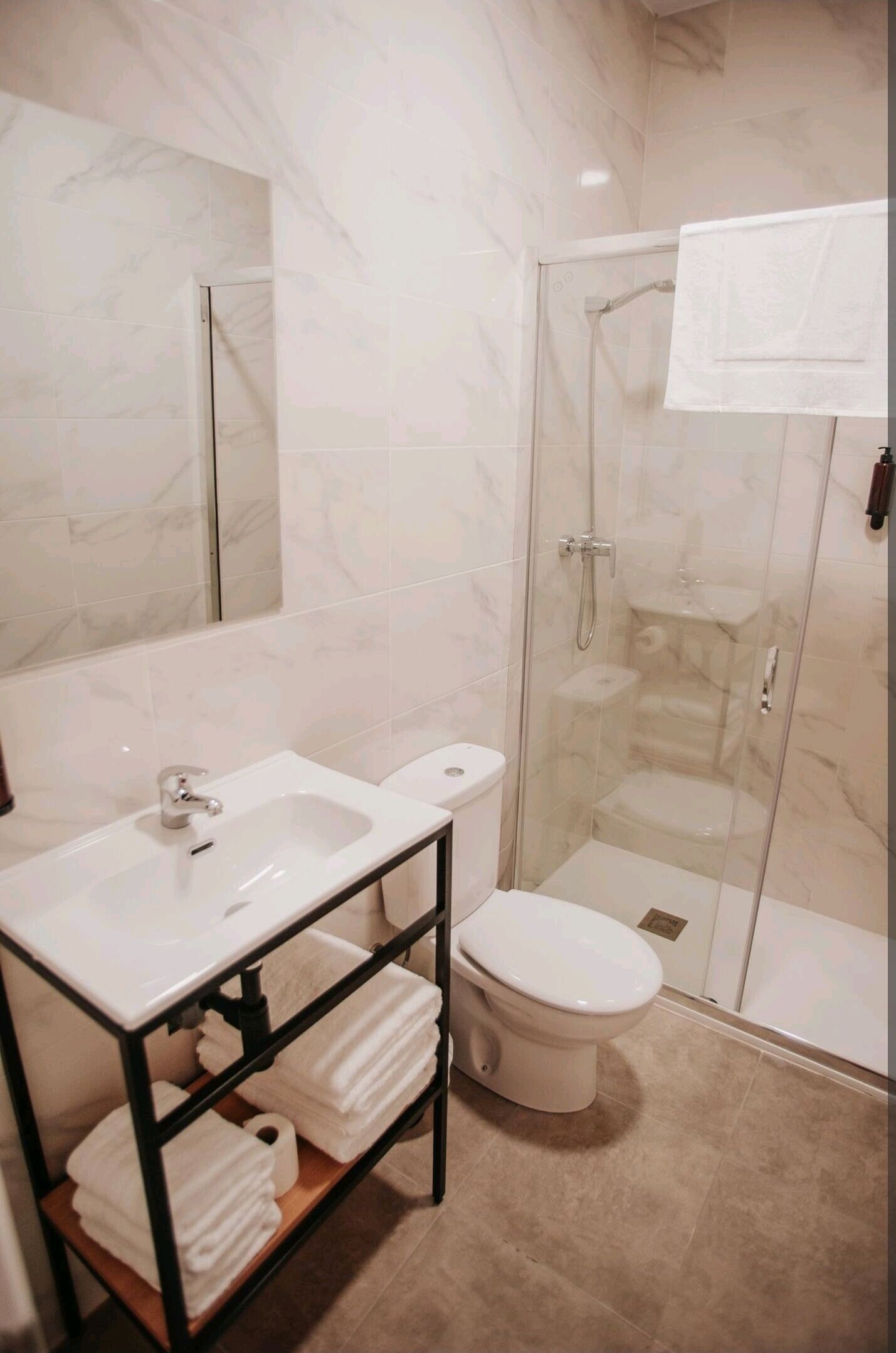 Un baño con ducha de vidrio, un lavabo blanco con espejo y un inodoro.