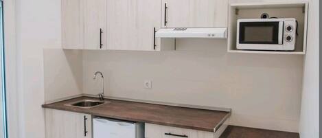 Una cocina moderna con armarios blancos, microondas integrado, un lavabo y una mesa de comedor de madera.