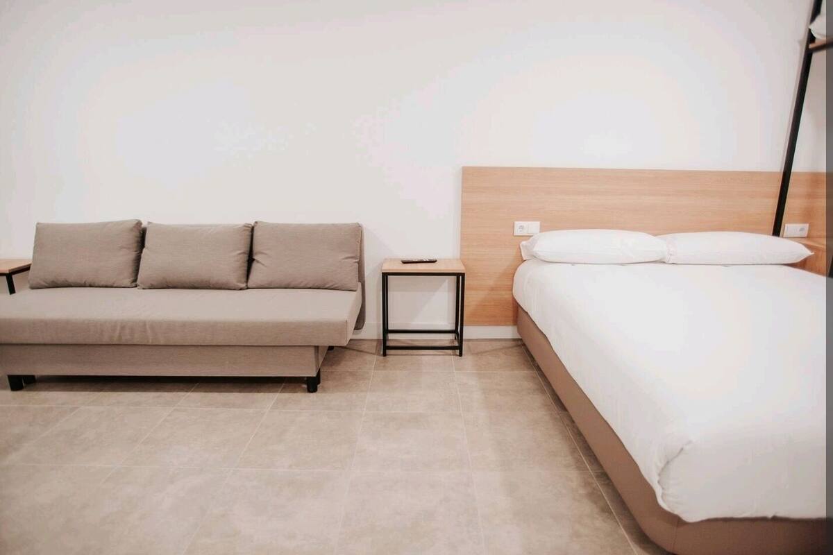 A modern bedroom with a sofa bed, a single bed, and a small bedside table.