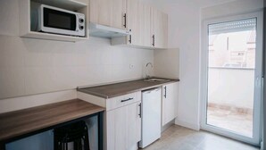 A compact kitchen with white cabinets, a microwave, a sink, and a sliding glass door to a balcony. - Polorooms Vara (Zaratan)