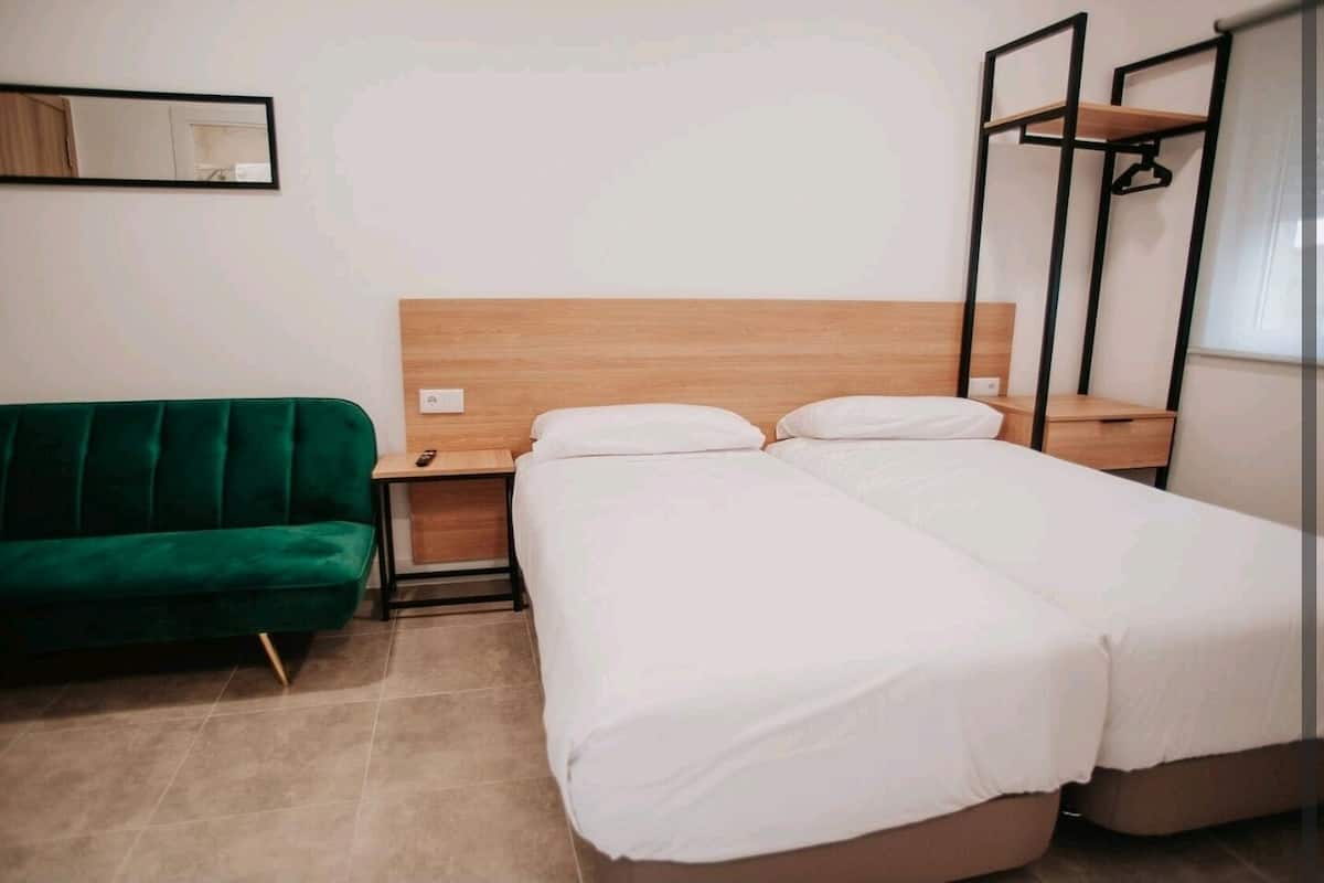 A hotel room with a wooden headboard, two beds, a green sofa, a nightstand, and a mirror.