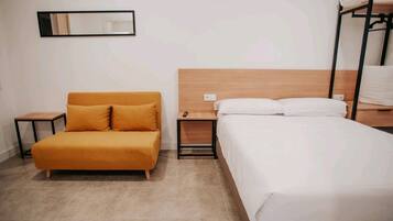 Habitació d'hotel amb sofà, llit, taulella al costat del llit i un llit superposat.