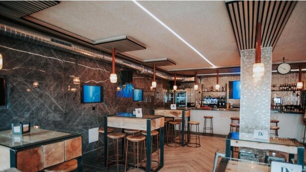 A modern bar area with wooden stools, a bar counter, and a television screen. - Polorooms Vara (Zaratan)