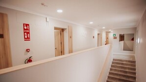 A hotel corridor with wooden doors, a handrail, and emergency exit signs. - Polorooms Vara (Zaratan)