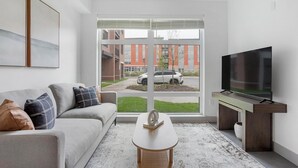 Ein modernes Wohnzimmer mit einem grauen Sofa, einem Couchtisch und einem Fernseher auf einem Holzboden.
