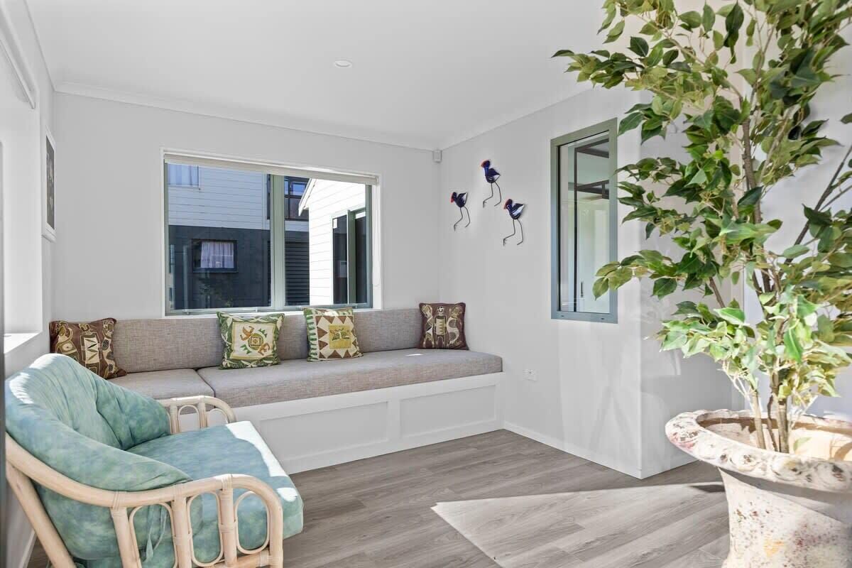 A modern living room with a built-in bench, a large potted plant, and a window with blinds.