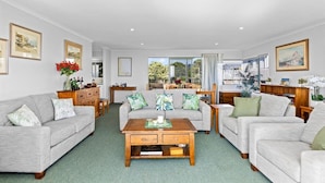 A spacious living room with a sofa set, a coffee table, and a view of the outdoors. - Oceanview on Broadway (Waihi Beach)