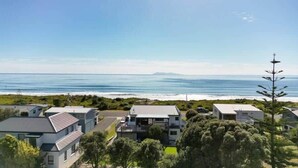 A coastal residential area with houses, a clear view of the ocean, and a prominent tree. - Oceanview on Broadway (Waihi Beach)