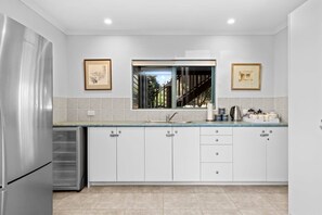 A modern kitchen with white cabinets, a stainless steel refrigerator, a window with a view, and framed pictures on the wall.