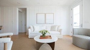 A modern living room with a white sofa, a patterned armchair, and a coffee table with a vase of flowers. - Allure by Mira-Mar (Wrightsville Beach)