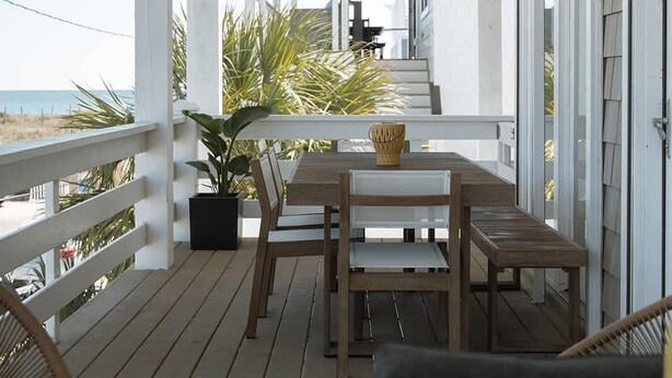 A covered outdoor area with a wooden table and chairs, a ceiling fan, and a view of the beach. - Allure by Mira-Mar (Wrightsville Beach)